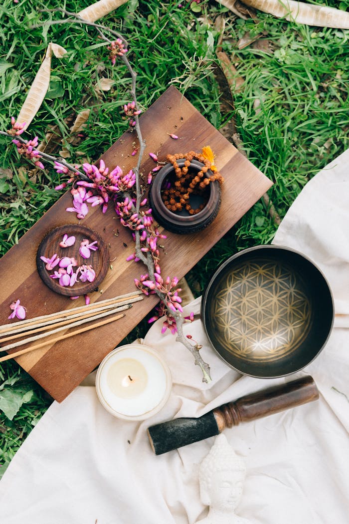 An overhead view of a singing bowl, incense sticks, and pink flowers for meditation, promoting relaxation.
